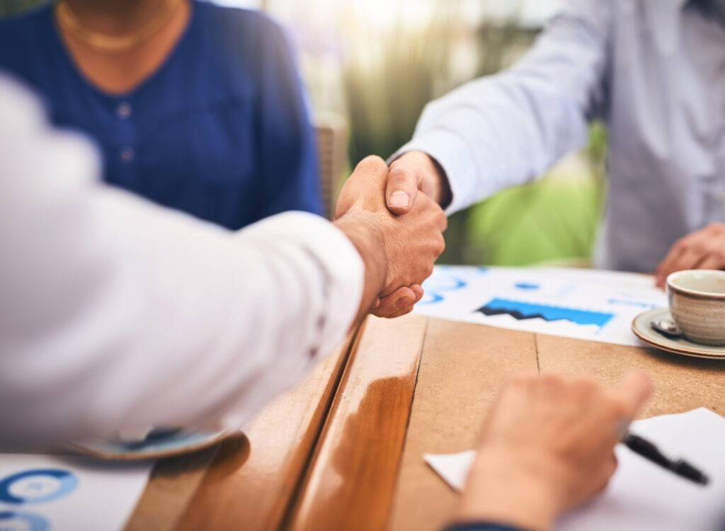 Business people shaking hands in a coffee shop during a teamwork and onboarding meeting in Lumberton.