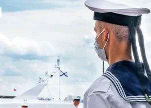 oung U.S. Navy sailor in full dress uniform wearing a protective medical mask, representing asbestos exposure risks in shipyards