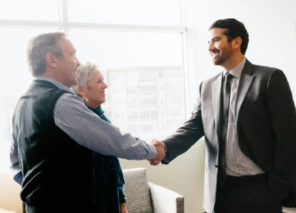 A professional attorney shaking hands with a senior client in a bright office, representing trust and legal partnership.