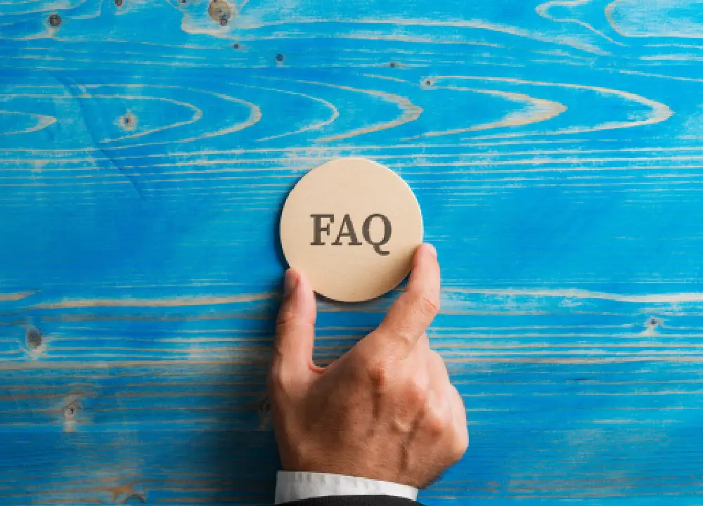 Hand holding a wooden circle with an FAQ sign on it.