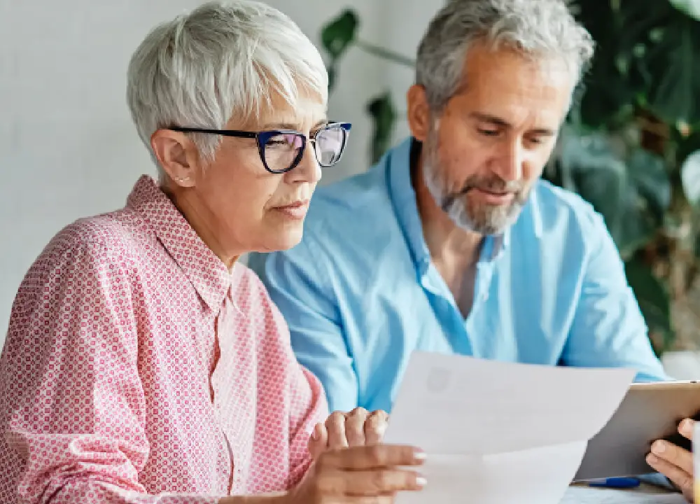 Senior couple at home reviewing medical bills and financial documents with a serious expression.