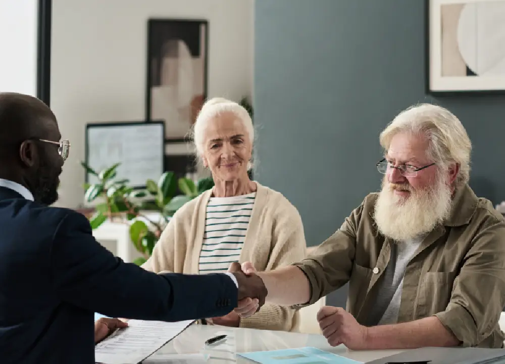 A senior man shaking hands with a legal professional in a bright office, symbolizing a new partnership.