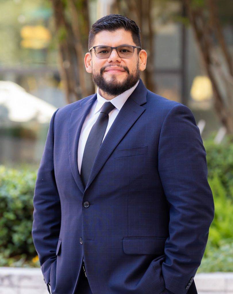 Ben Herrera, wearing a navy suit and glasses, outdoor professional headshot