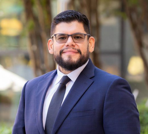 Outdoor professional headshot of a man in a navy suit and glasses